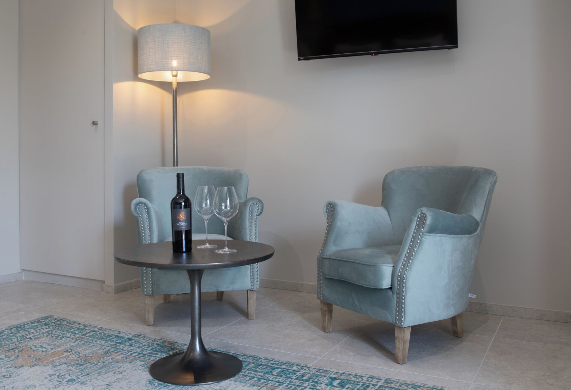 Una habitación con una mesa redonda, dos sillones, una botella de vino y dos copas de vino.