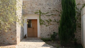 A stone-walled building with a wooden door, a narrow pathway, and a tall green tree. - Country House 'Fetget' with Mountain View, Private Pool and Wi-Fi (Illes Balears)