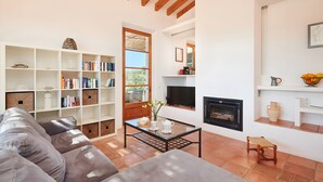 A living room with a sofa, a glass coffee table, a fireplace, and a bookshelf. - Country House 'Fetget' with Mountain View, Private Pool and Wi-Fi (Illes Balears)