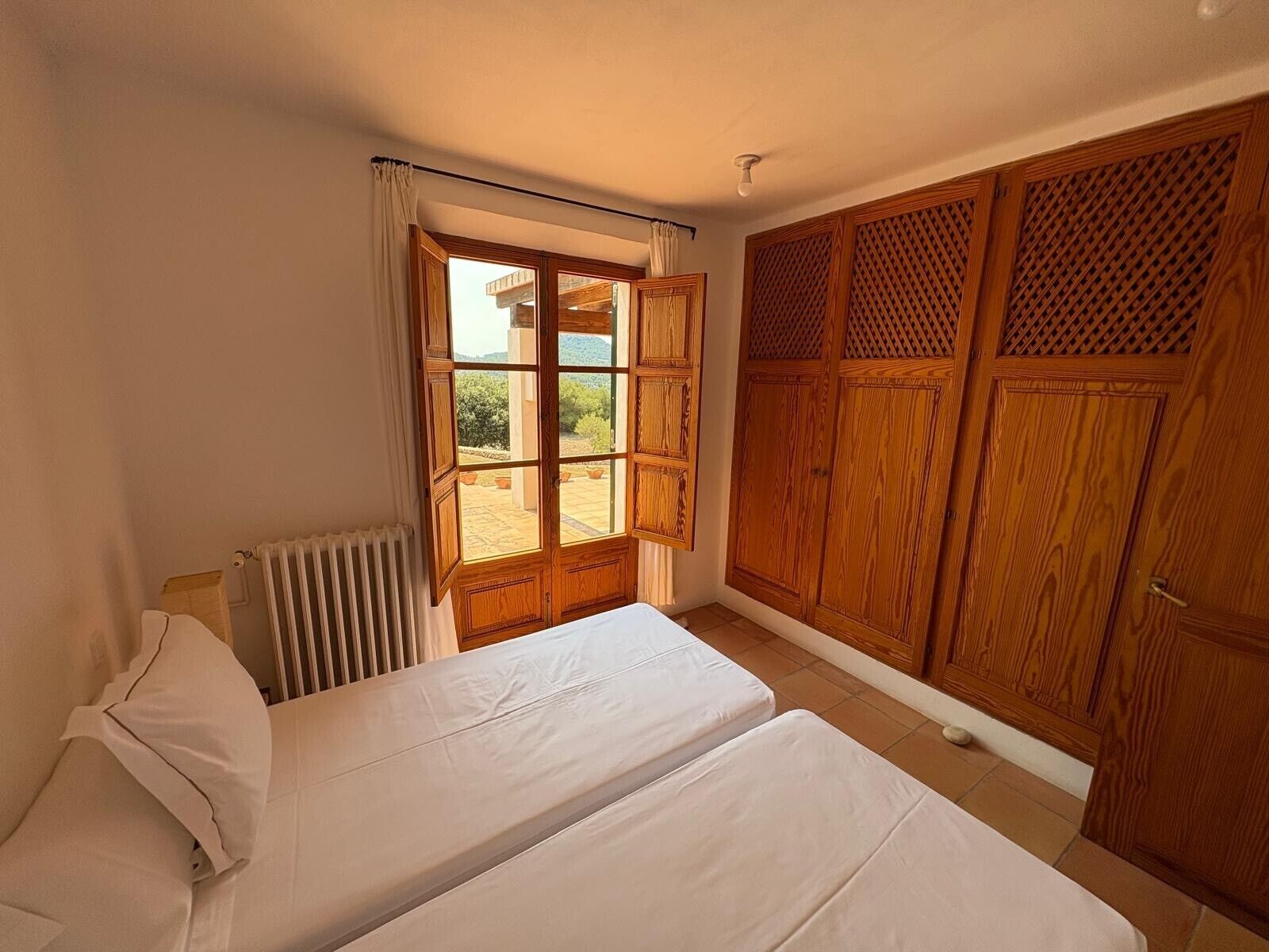 A bedroom with a bed, a radiator, a window with curtains, and wooden wardrobes.