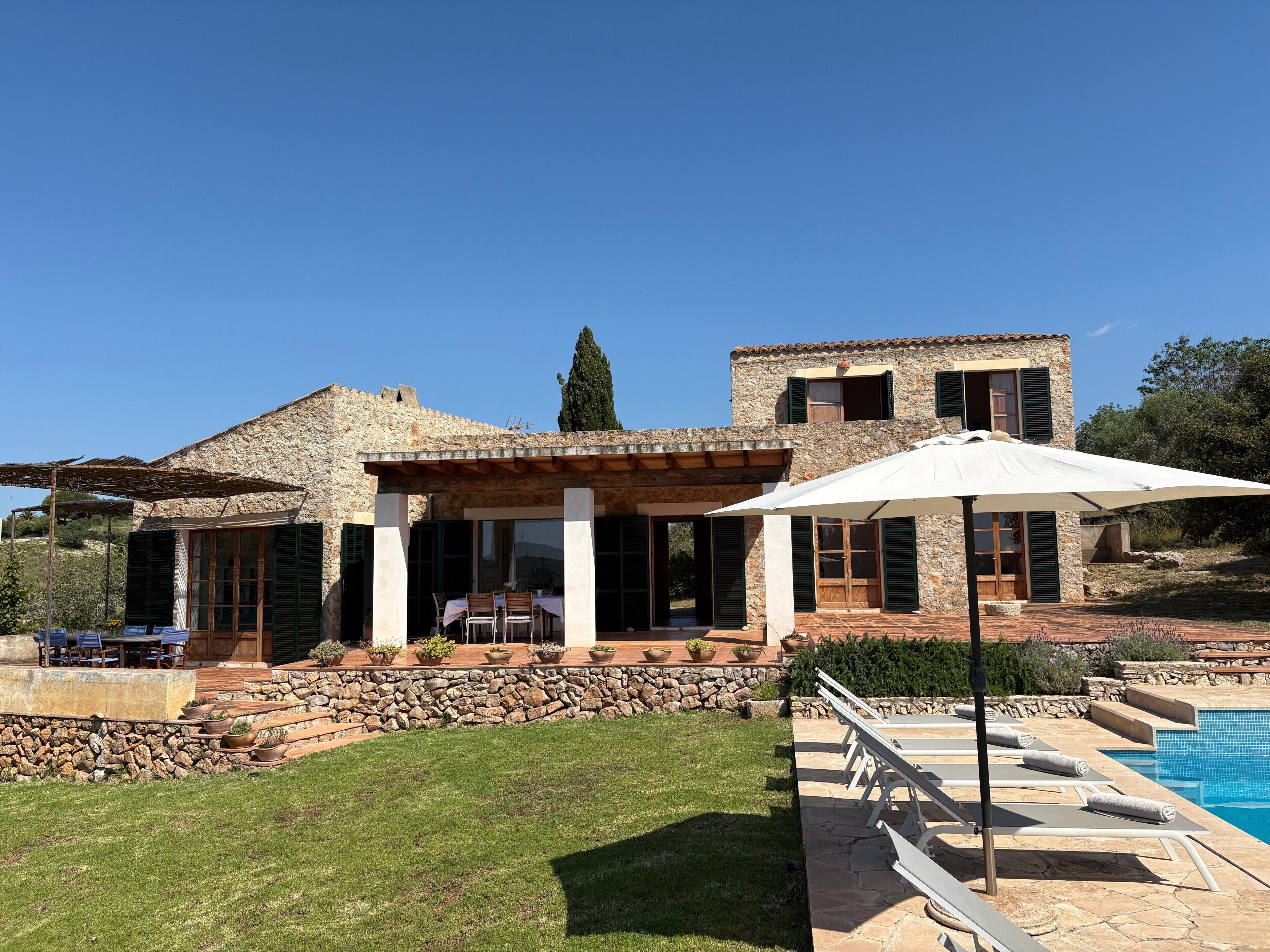 A stone house with a pool, outdoor seating, and a well-maintained lawn.