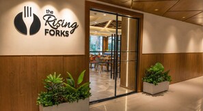 A restaurant entrance with a logo, wooden paneling, and potted plants. - Medalio Boutique Kota River Front (Kota)