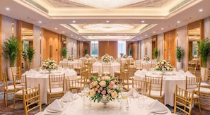 A banquet hall with round tables, gold chairs, and floral centerpieces.
