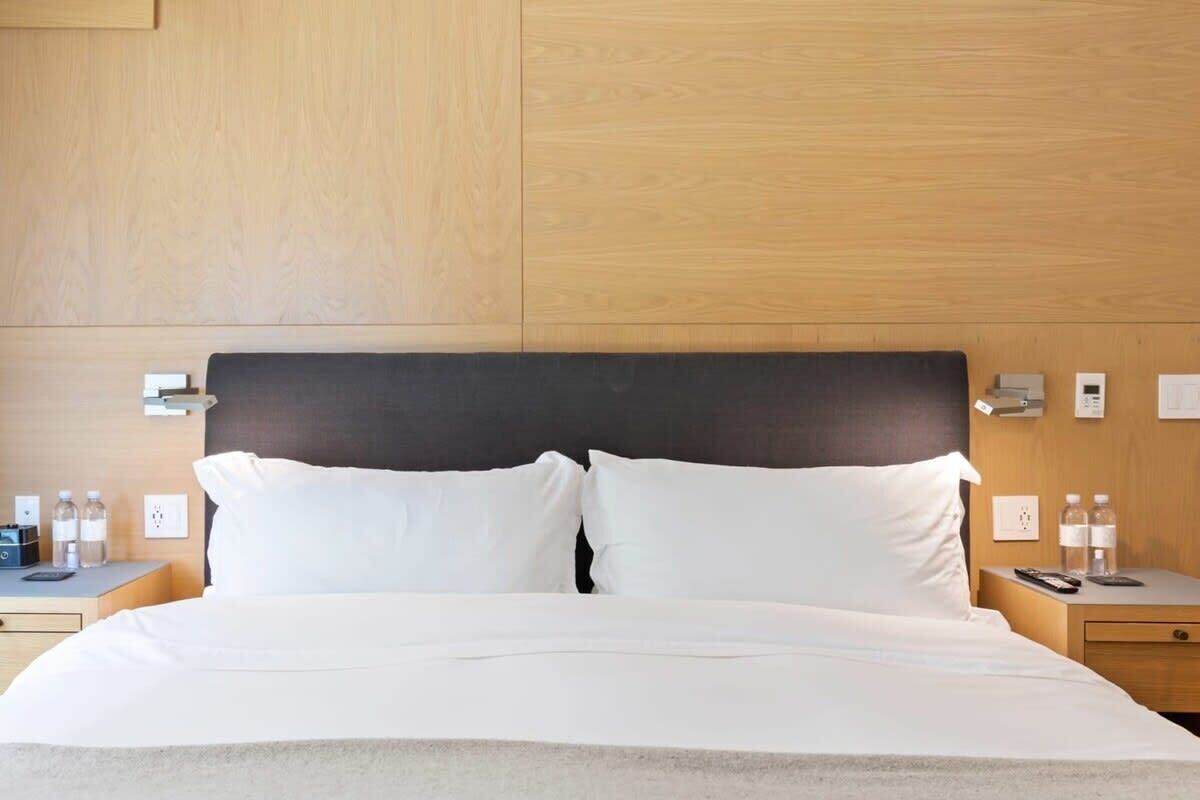 A hotel room with a bed, bedside tables, and wall-mounted lights.