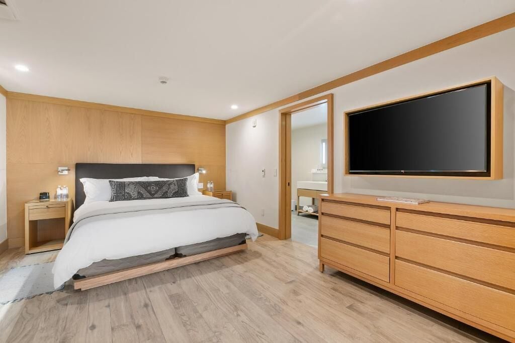 Ein modernes Schlafzimmer mit einem Bett, Nachttischen, einem Fernseher und einer hölzernen Kommode.