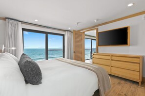 Un dormitorio moderno con una cama grande, un televisor montado en la pared y vistas al mar.