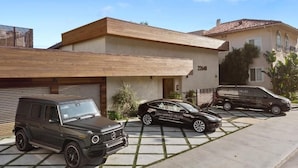 Ein modernes, zweistöckiges Haus mit Garage, einem geparkten SUV und einer Limousine.