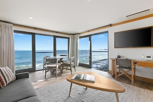 Habitación de hotel moderna con un amplio ventanal con vistas al mar, un televisor de pantalla plana, un escritorio y una zona de estar cómoda.