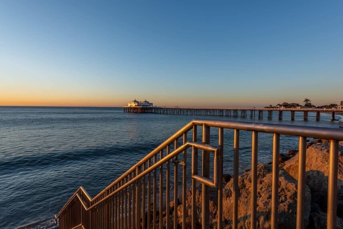 A coastal scene with a pier extending into the water, a staircase leading down to the water, and a building on the pier.