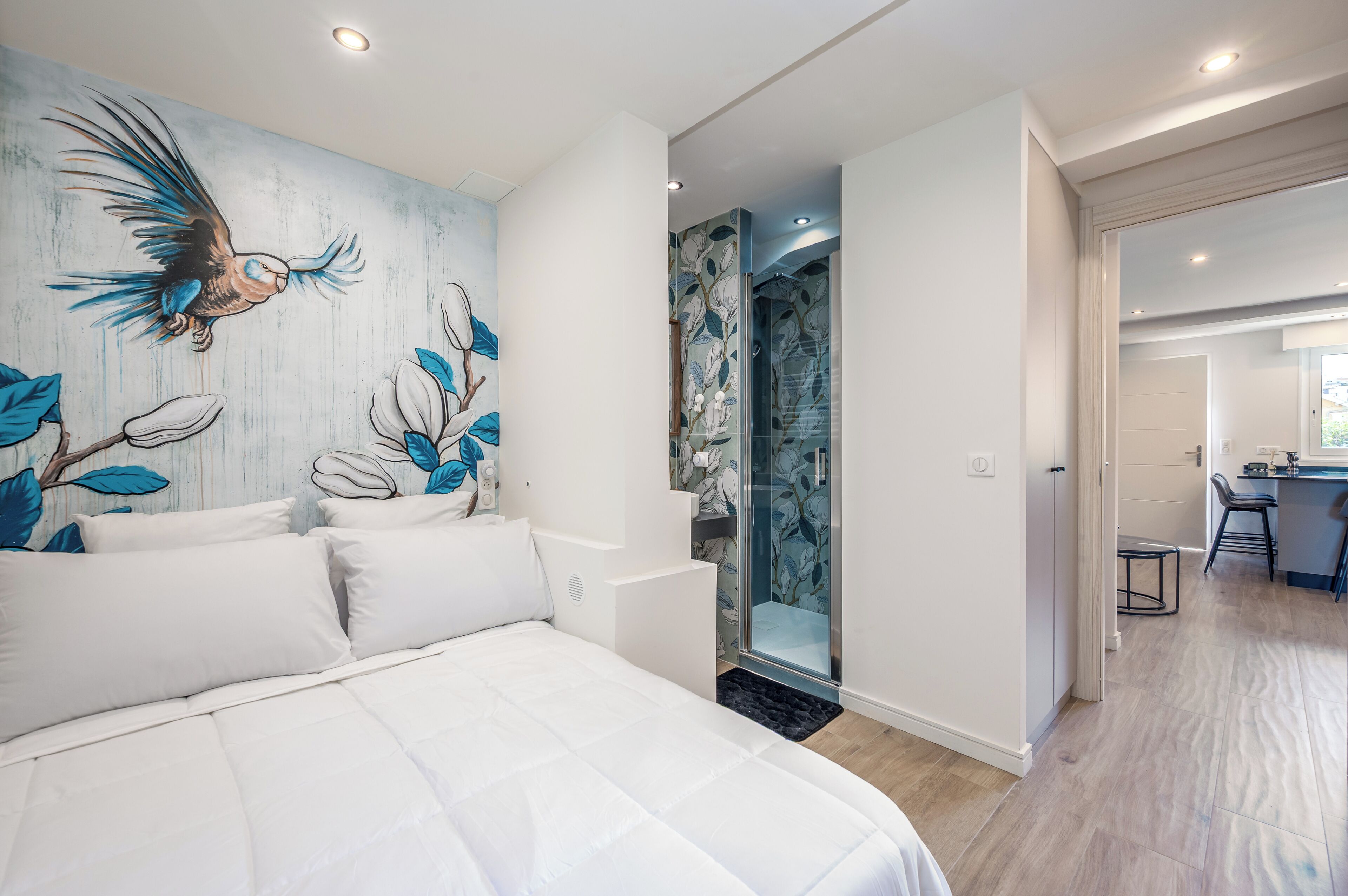Een moderne slaapkamer met een groot bed, een douche met glazen deur en een muurschildering.
