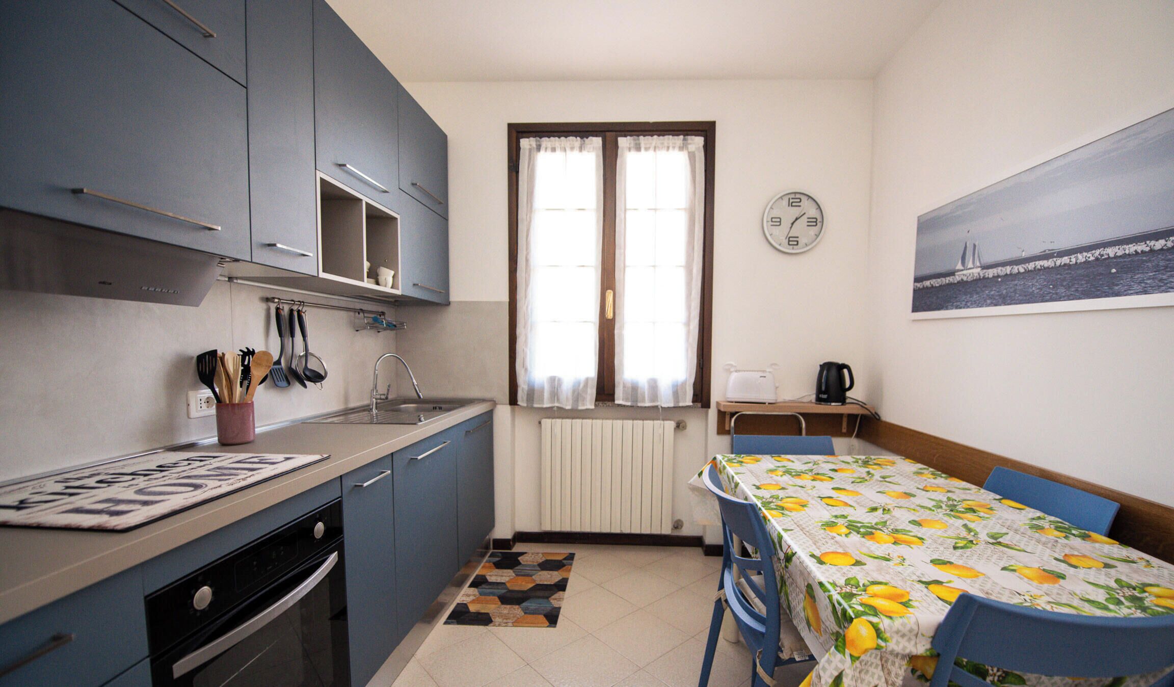 A compact kitchen with a dining area, a radiator, and a clock on the wall.