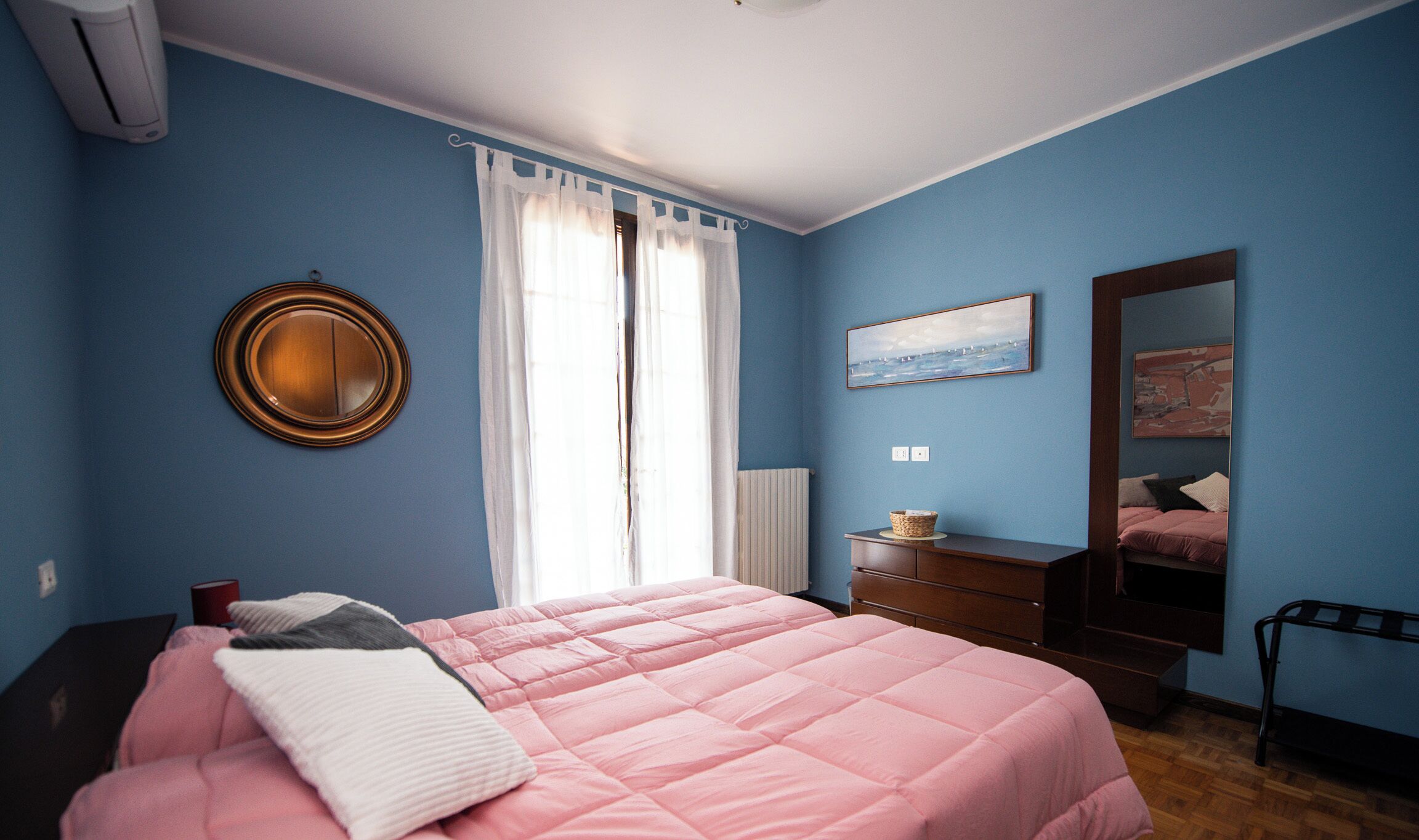 A bedroom with a bed, dresser, mirror, and artwork on the wall.