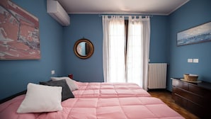 Een slaapkamer met een bed, een spiegel, een raam met gordijnen, een radiator en kunst aan de muren.