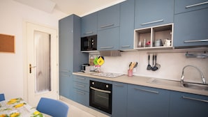 Een compacte keuken met blauwe kastjes, een magnetron, een oven en een spoelbak.