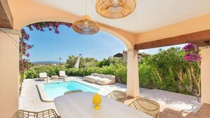 An outdoor pool area with lounge chairs and a table, surrounded by greenery and a clear sky. - ELITE COLLECTION- DOMO MEA (Pittulongu)