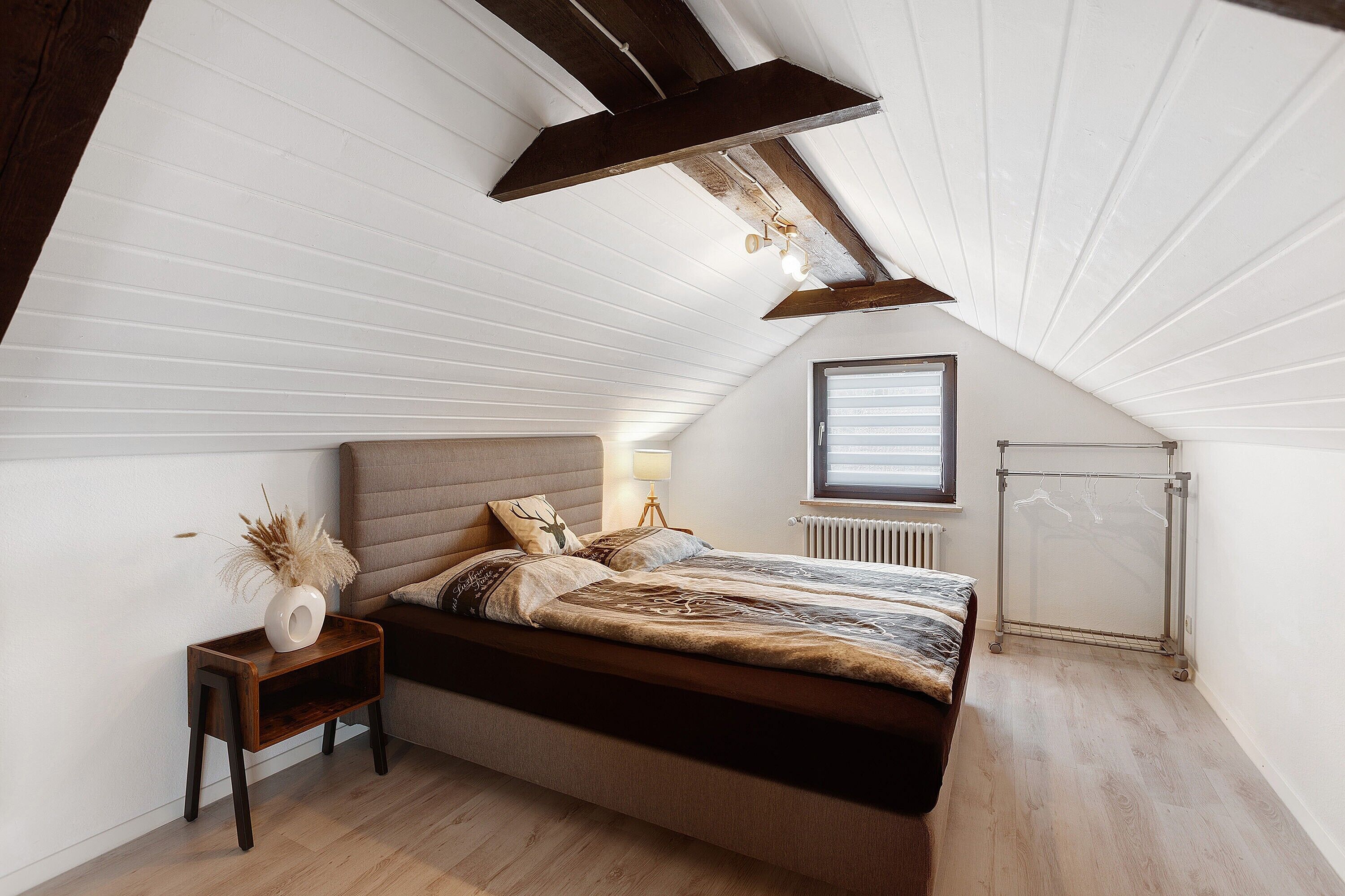 Een slaapkamer met een schuine kap, een bed met hoofdeinde, een nachtkastje met lamp en een radiator.