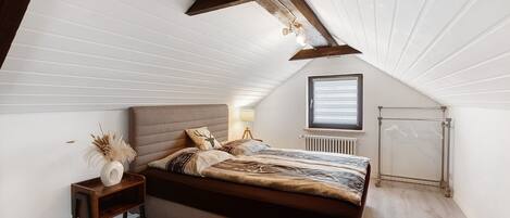Een slaapkamer met een schuine kap, een bed met hoofdeinde, een nachtkastje met lamp en een radiator.