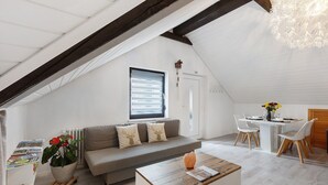 Un dormitorio estilo loft con techo inclinado, un sofá decorado con cojines, una mesa de comedor con sillas y una planta en maceta.