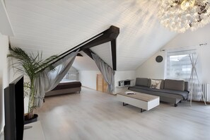 Un dormitorio tipo loft moderno con techo inclinado, cama empotrada, sofá, mesa de centro, televisor y una planta grande en maceta.