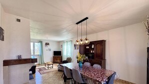 A dining area with a table, chairs, a chandelier, and a television in the background. - Charming house, terrace, pets allowed - 4 guests (CLERMONT DE BEAUREGARD)