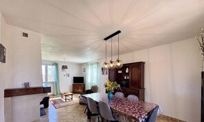 Ein Essbereich mit Tisch, Stühlen, einer Chandelierleuchtre und einem Fernseher im Hintergrund.