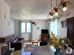 Ein Wohnzimmer mit einer Couch, Fernseher, Esstisch und Zimmerpflanzen.