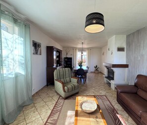 Ein Wohnzimmer mit Sofa, Sessel, Esstisch und Kamin.