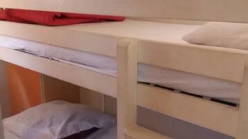 Una cama nido con ropa blanca y un objeto rojo en la parte superior.