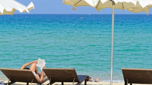 A beach scene with lounge chairs and umbrellas, a clear blue sea, and a thatched roof structure. - Chalet with terrace - 3 guests (Algajola)