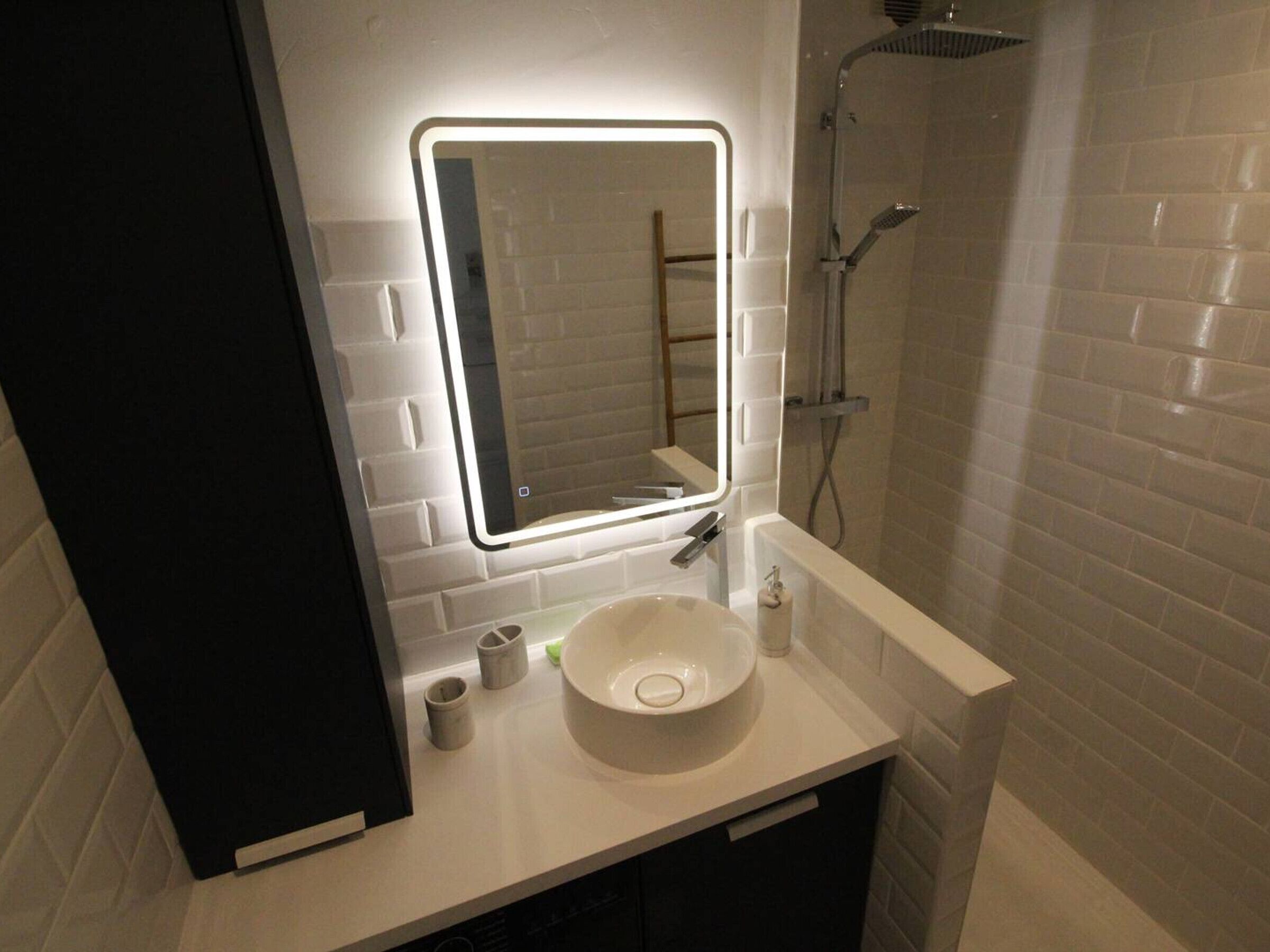 A bathroom with a white sink, a mirror with a light, and a shower.