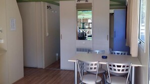 A room with a dining table and chairs, a window with curtains, and a door leading to another room. - Cozy chalet with terrace - 5 guests (Algajola)