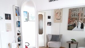 Una sala de estar moderna con piso de madera, un sofá blanco, una pequeña mesa redonda con una planta y una estantería.