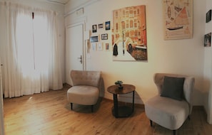 A room with a wooden floor, two armchairs, a small round table, and a door with white curtains. - ‘La Guglia - Guglia House’ Apartment with Wi-Fi and Air Conditioning (Venezia)