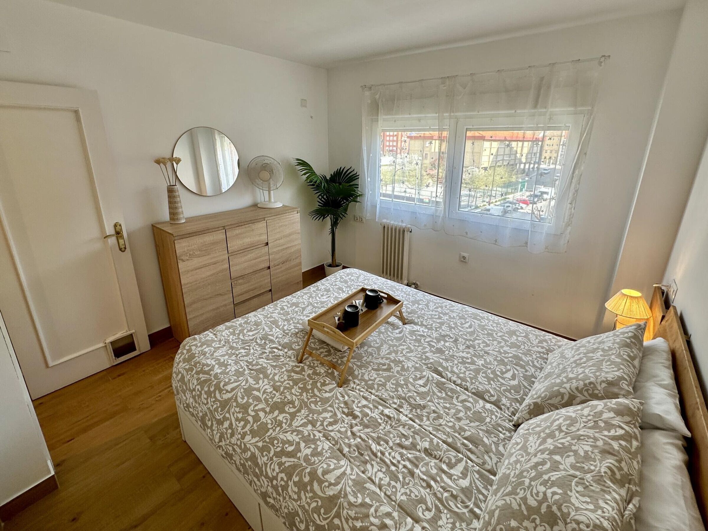 A bedroom with a bed, bedside table, dresser, mirror, window, and radiator.