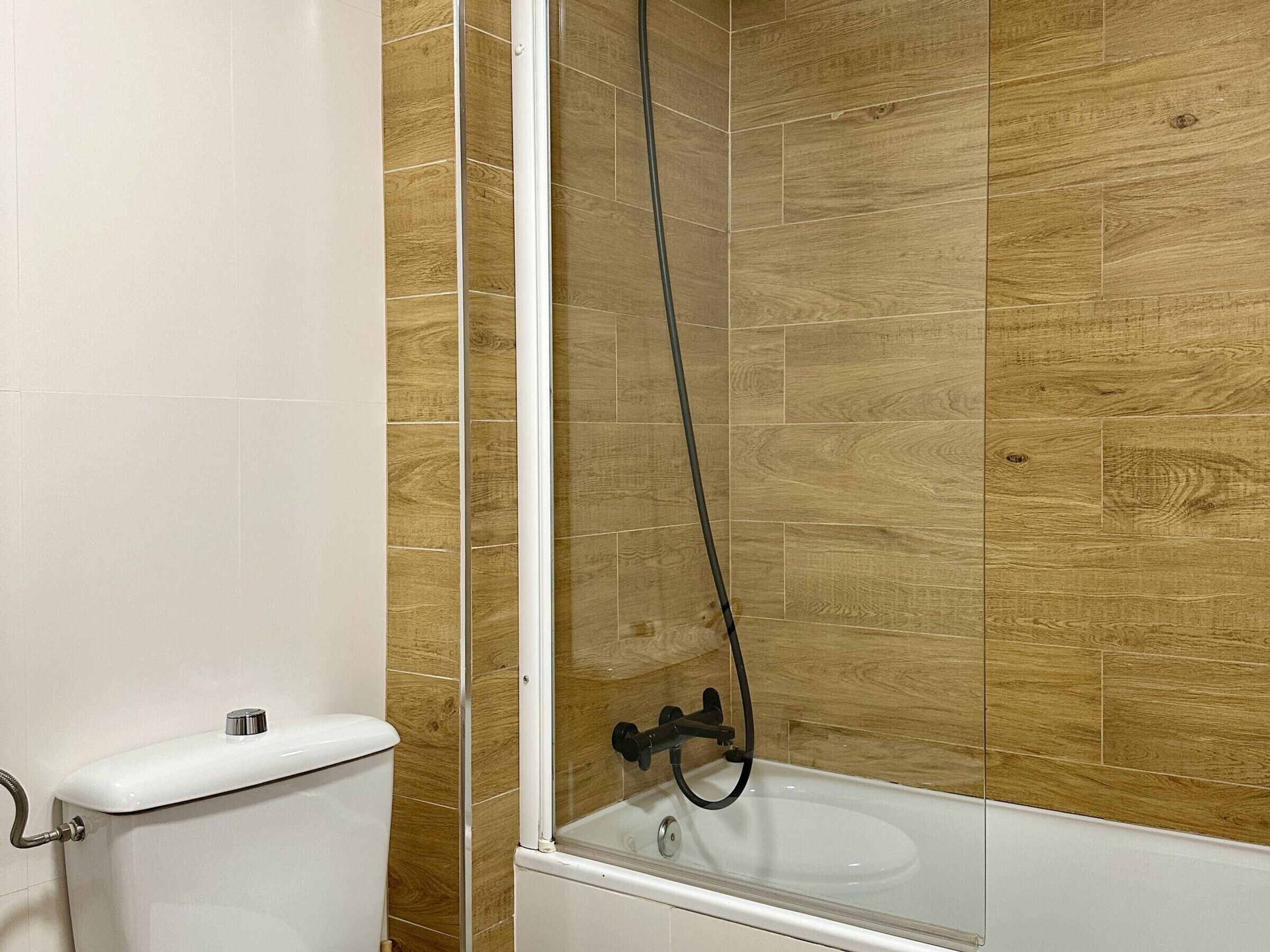 A bathroom with a toilet, a glass-enclosed shower, and wooden wall tiles.