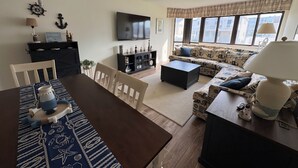 A living room with a wooden dining table, sofa, TV, and decorative items.