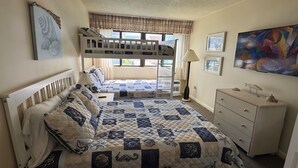A bedroom with bunk beds, a bedside table with a lamp, a dresser, and a large painting on the wall.