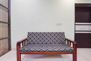 A wooden chair with a patterned cushion in a room with a plain wall and a door. - Classic With Twin Bed Sairaj Lodging (Satara)