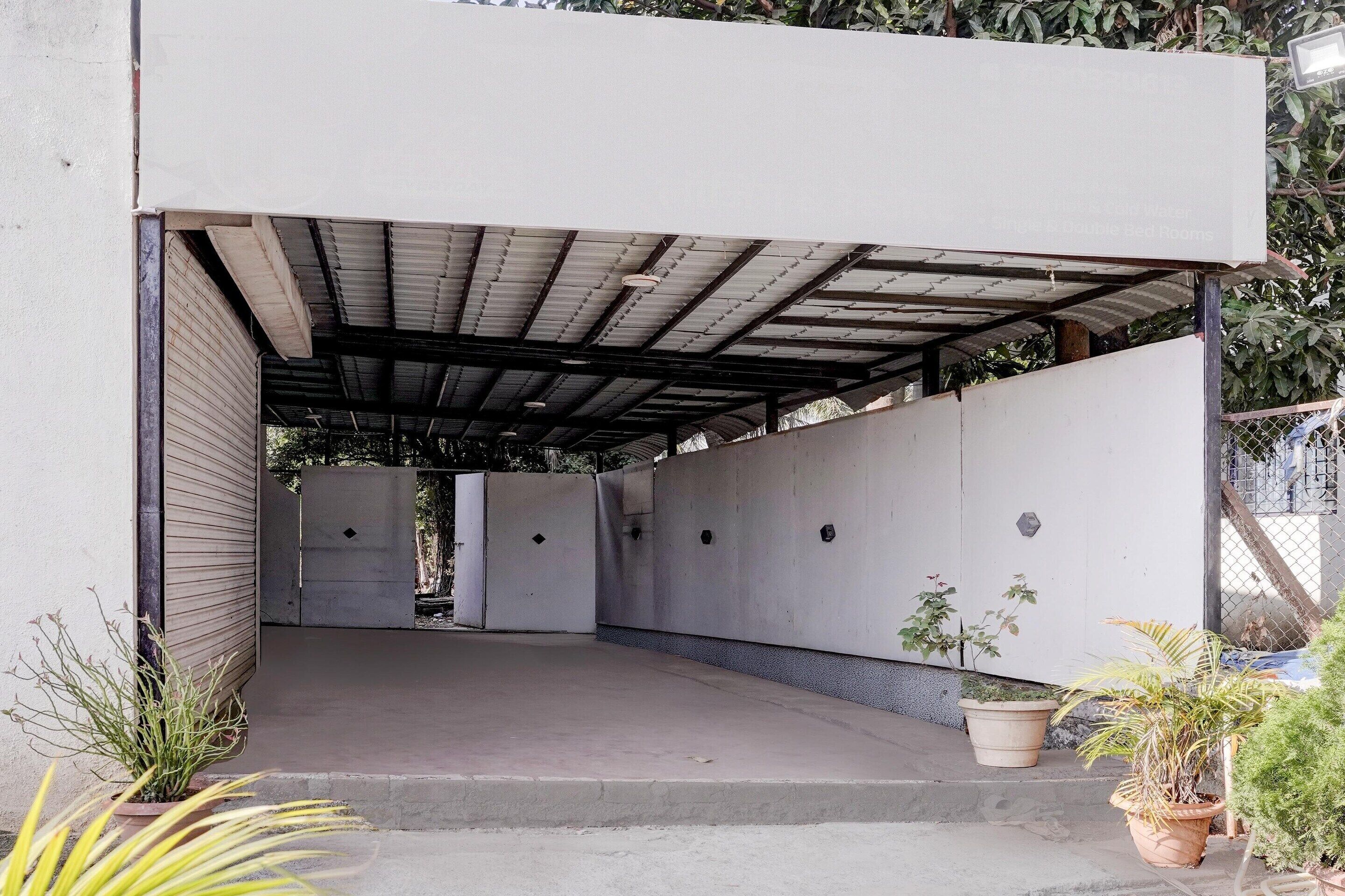 A covered outdoor area with a concrete floor, potted plants, and a metal roof structure.