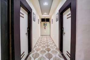 A hallway with patterned flooring, doors on either side, and a fire extinguisher mounted on the wall. - Classic With Twin Bed Sairaj Lodging (Satara)