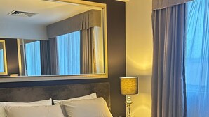 A hotel room with a large bed, a bedside lamp, a mirror, and a window with curtains. - The Heritage Bank Apartment (Melbourne)