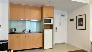 A compact kitchen with wooden cabinets, a microwave, a refrigerator, a sink, and a kettle. - The Heritage Bank Apartment (Melbourne)