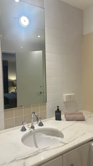 Un bagno con uno specchio grande, un lavandino con un solo rubinetto, un dispenser di sapone e un asciugamano sul ripiano.