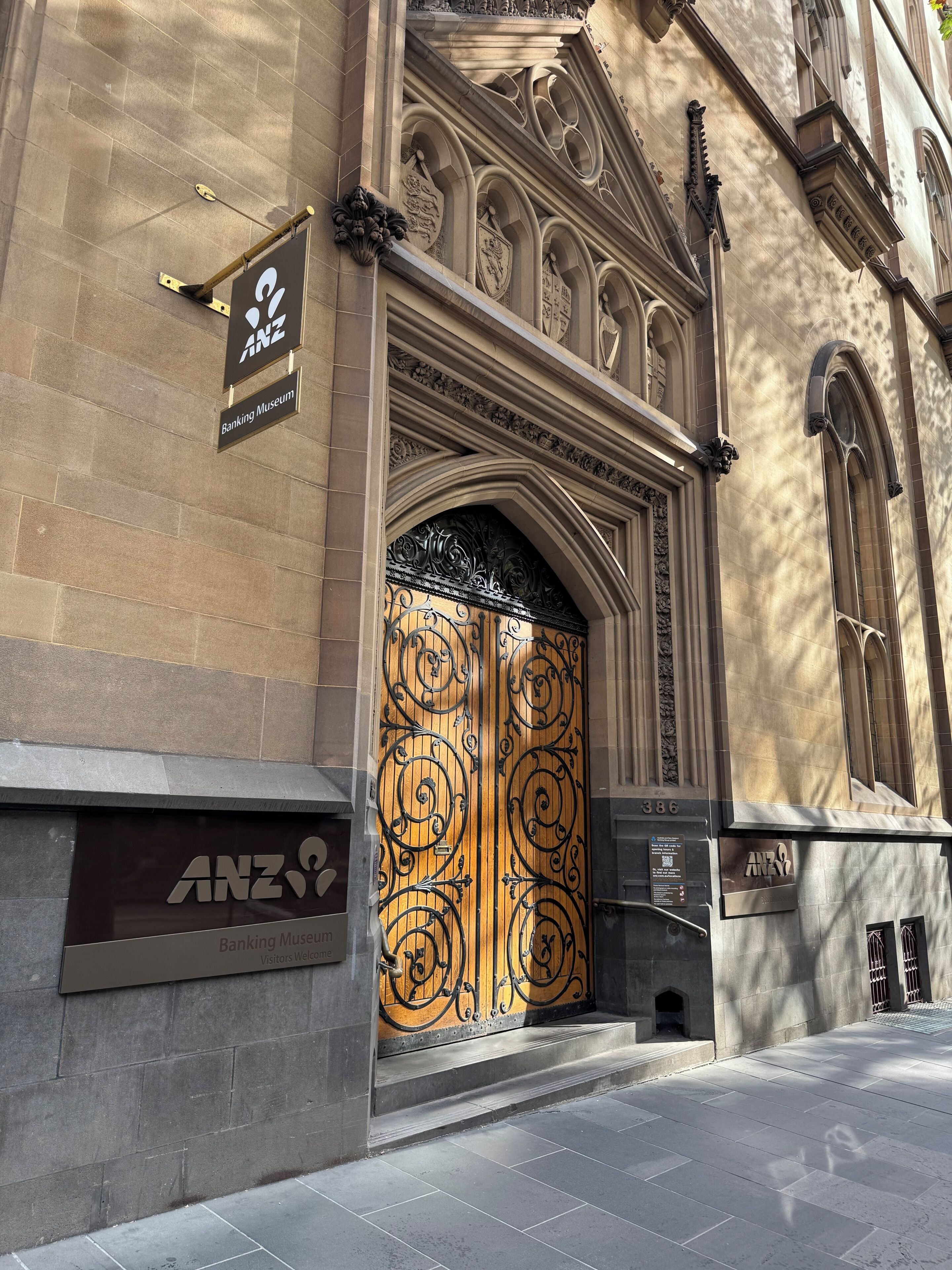 Entrada de un edificio con un gran portón decorativo, un cartel del Museo Bancario ANZ y fachada de piedra.