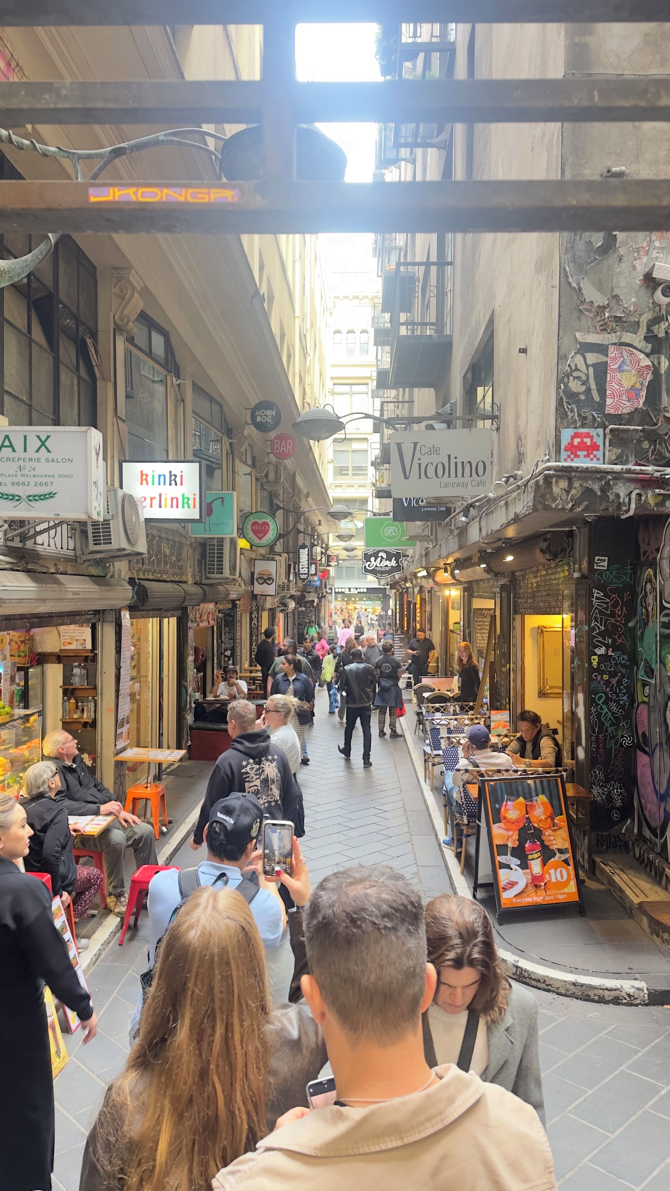 A bustling street with shops and cafes, narrow pedestrian pathways, and people walking.