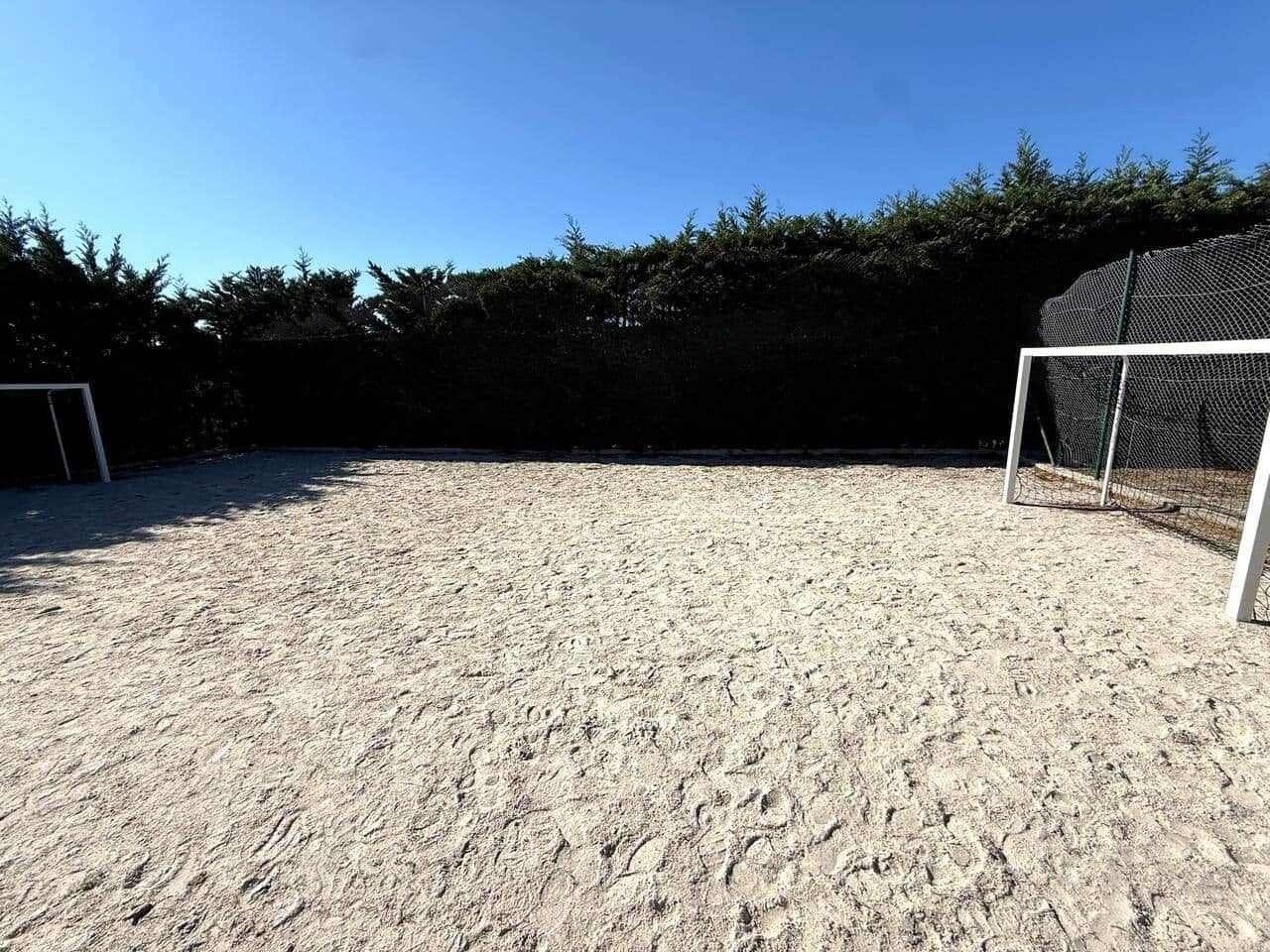 A sandy outdoor area with a soccer goal and a fence.