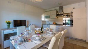 A modern kitchen with built-in appliances, a dining area with a table set for four, and a television on a cabinet. - Modern apartment with beautiful sea views (Crikvenica)