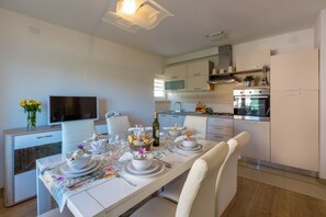 A modern kitchen with built-in appliances, a dining area with a table set for four, and a television on a cabinet. - Modern apartment with beautiful sea views (Crikvenica)