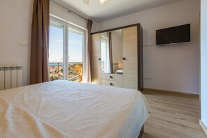 A bedroom with a bed, a dresser, a TV, and a balcony with a view. - Modern apartment with beautiful sea views (Crikvenica)
