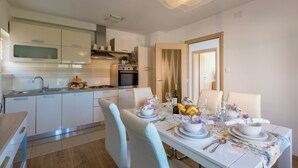 A modern kitchen with white cabinets, a dining table set with plates, bowls, and cutlery, and a large mirror above the table. - Modern apartment with beautiful sea views (Crikvenica)